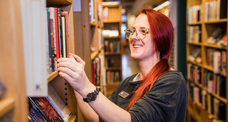 En kvinna som lämnar en bok i bokhyllan och ler